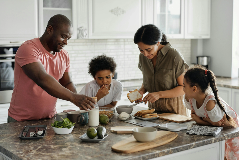 A family of four around a kitchen table making breakfast together